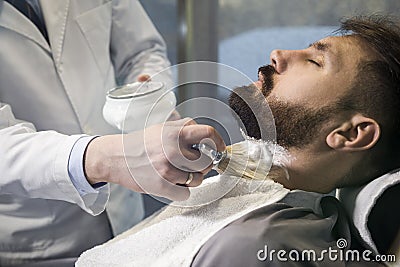 Close up of a bearded brown haired businessman sitting at a barber shop in a chair. Stock Photo