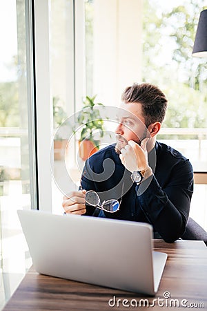 Close up of a bearded businessman glasses in hand and sitting at his laptop and look in the window. Stock Photo