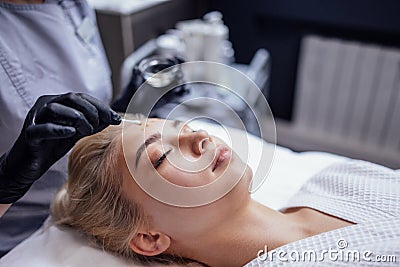 Close up of beautician applies anti-aging cream in black gloves to face of female client in spa salon or clinic Stock Photo