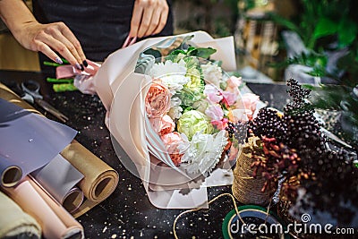Close up of beautiful bouqette of flowers lying on table. There are rolls of paper and flowers. Woman touch bouquet with Stock Photo