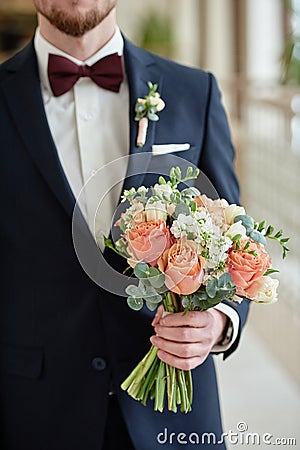 Close up of beautiful bridal bouquet of coral roses and greenery in groom& x27;s hand indoors, copy space. Stock Photo