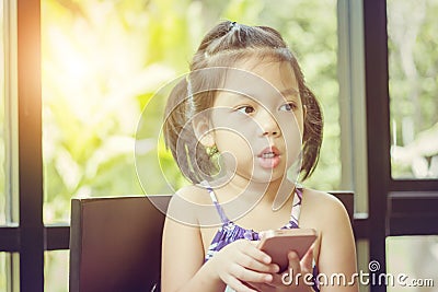 Close up of beautiful little cute girl looking up thinking and holding smartphone, Happy kid concept Stock Photo