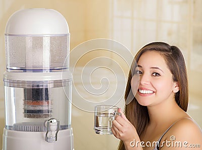 Close up of a beautiful smiling woman holding a glass of water, with a filter system of water purifier on a kitchen Stock Photo