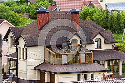 Close-up of big new comfortable two-storied new cottage with green tile roof, big yard, plastic windows and high chimneys in mode Stock Photo