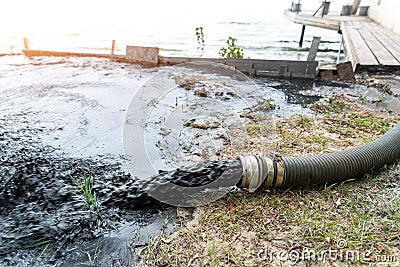 Close-up big pipe of power pump machine pouring mud sludge waste water with sand and silt on ground. Sand-wash and coast Stock Photo