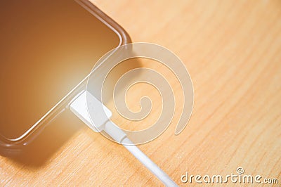 Black color mobile smart phone charging on wooden table. Stock Photo