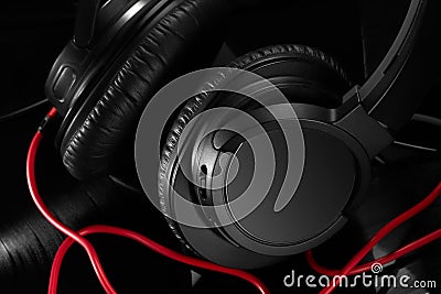 Close-up of black headphones with a red wire on a black matte background of vinyl records. Stock Photo