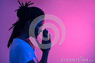 Close up of black man with dreadlocks praying on purple background Stock Photo