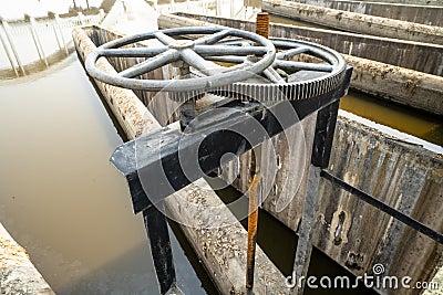 Close-up of black metal cogwheel controlling floodgate with texts in Thai language meaning `the property of` on one side. Stock Photo