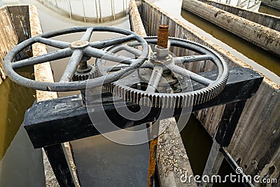 Close-up of black metal cogwheel controlling floodgate with texts in Thai language meaning `the property of` on one side. Stock Photo