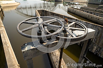 Close-up of black metal cogwheel controlling floodgate with texts in Thai language meaning `the property of` on one side. Stock Photo