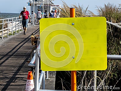 Close-up of a blank yellow sign at the entrance to a wooden pier on a sunny day at the beach Editorial Stock Photo