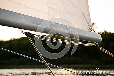 Close up on the boom mast of a sailing yacht, with sail and rigging ropes, and river or lake coast in the background Stock Photo