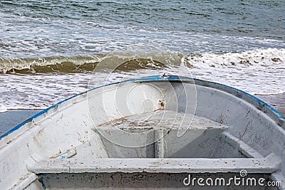 Close-up of the bow of rowing fishing boat on sandy shore of a coastal beach with sea water in background Stock Photo