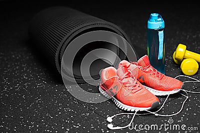 Close-up of bright training shoes, dumb-bells, rubber mat, blue bottle, and headphones on a black spotted background. Stock Photo