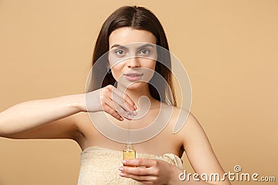 Close up brunette half naked woman 20s with perfect skin, nude make up apply oil from bottle on face isolated on beige Stock Photo