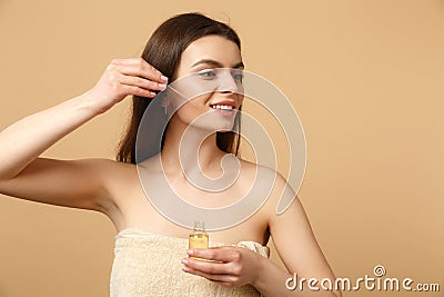 Close up brunette half naked woman 20s with perfect skin, nude make up apply oil from bottle on face isolated on beige Stock Photo