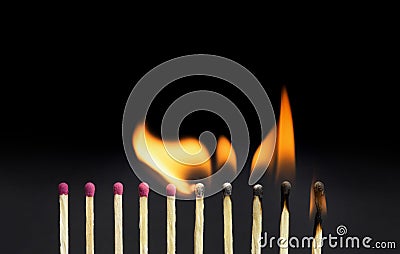 Close-up of burning matches igniting other matchsticks in a row against a black background Stock Photo