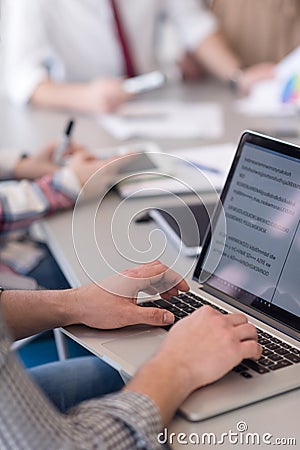 close up of business man hands typing on laptop with team on meeting in background Stock Photo
