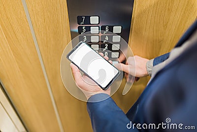 Man hands holding blank screen mobile phone while using elevator control panel Stock Photo