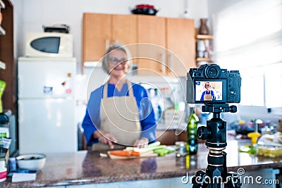 Close up of camera filming a mature woman or senior cooking and doing live or video for her social networks and medias - Stock Photo