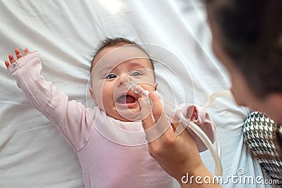 Close up of caring mother with nasal pump to clean her baby's nose. Baby lying in bed Stock Photo