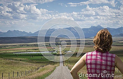 Close up of caucasian woman facing toward a long dirt road in summer. Stock Photo