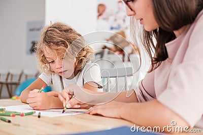 Child with an autism spectrum disorder and the therapist by a table drawing with crayons during a sensory Stock Photo