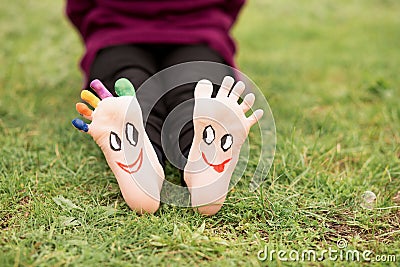 Close up of child human pair of feet painted with smiles outdoor in park Stock Photo