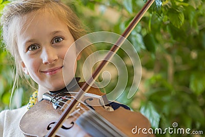 Close up of a child playing violin on green background. Portrait of girl with string and playing violin. Portrait of the little Stock Photo