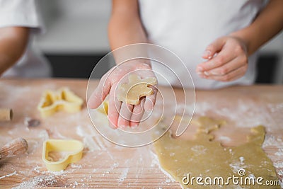 Close-up of a child`s palm with a piece of raw dough biscuits resembling a bear, in the background a kitchen table soaked in flou. Stock Photo