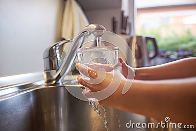 Close up of children hands, pouring glass of fresh water from tap in kitchen Stock Photo