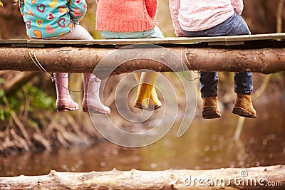 Close Up Of Children's Feet Dangling From Wooden Bridge Stock Photo