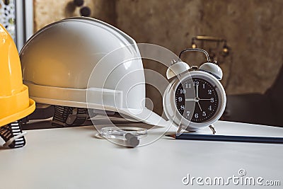 Close up of clock and engineering safety helmet on blueprint table. Architecture and engineering equipment concept. Construction Stock Photo