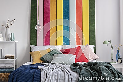 Close-up of a colorful bed with cushions and blankets standing against white wall with striped painting in bedroom interior. Real Stock Photo