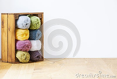 Close-up of a colorful yarn stack in a wooden crate by a white wall and copy space. Real photo. Stock Photo