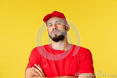 Close-up of confident handsome bearded delivery guy, male courier in red uniform cap and t-shirt, look tough and serious Stock Photo