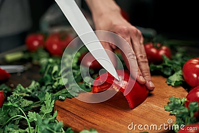 cook slicing paprika on a wooden chopping board. Stock Photo