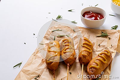 Close-up of corn dogs with mustered sauce and herb on paper bag by tomato sauce in bowl Stock Photo
