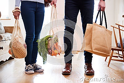 Close Up Of Couple Returning Home From Shopping Trip Carrying Groceries In Plastic Free Bags Stock Photo