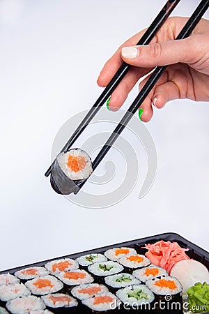 Close-up cropped photo shot of women`s hand person hold chopsticks delicious sushi rolls served on plate with white background Stock Photo