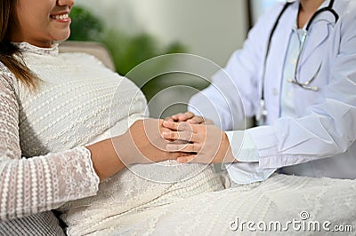 Asian pregnant woman is reassured by a professional female doctor, touching her belly Stock Photo