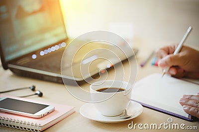 Close up cup of coffee and smart phone with hand of business man using laptop computer and write notebook on wooden desk office w Stock Photo