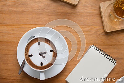 Close up of A Cup hot latte art coffee drawn an o`clock business concept on wooden table with note book Stock Photo