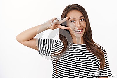 Close-up cute friendly-looking stylish young brunette in striped t-shirt showing peace, victory sign near eye smiling Stock Photo