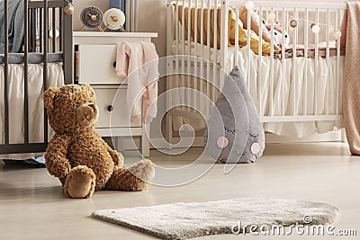 Close-up of a cute teddy bear and a gray raindrop pillow on the floor of a scandi bedroom interior for twins. Real photo Stock Photo