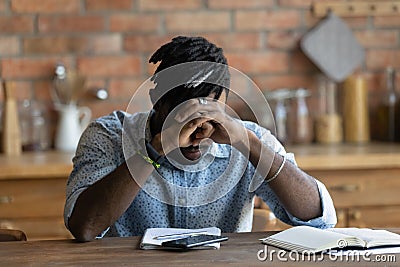Close up depressed exhausted African American man sitting at table Stock Photo