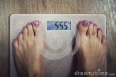 Close up of digital bathroom scale with female bare feet on it showing 55,5 kilogram on display. Woman standing on Stock Photo