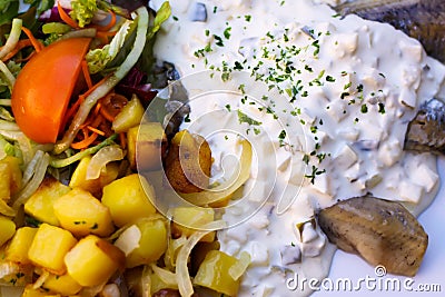 Close up of dish with young salted herring Matjes, white cream sauce with parsley and onions, baked potatoes and fresh salad Stock Photo