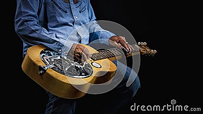 Close-up of a Dobro guitar resting on the lap of a musician dressed in cowboy attire on dark backdrop Stock Photo